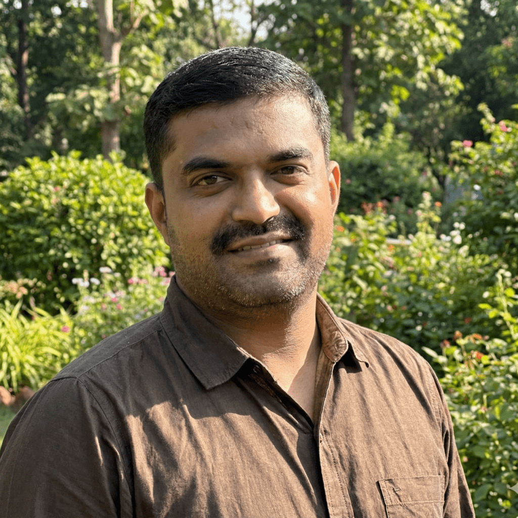 A man in a brown shirt standing in a sun-dappled garden.